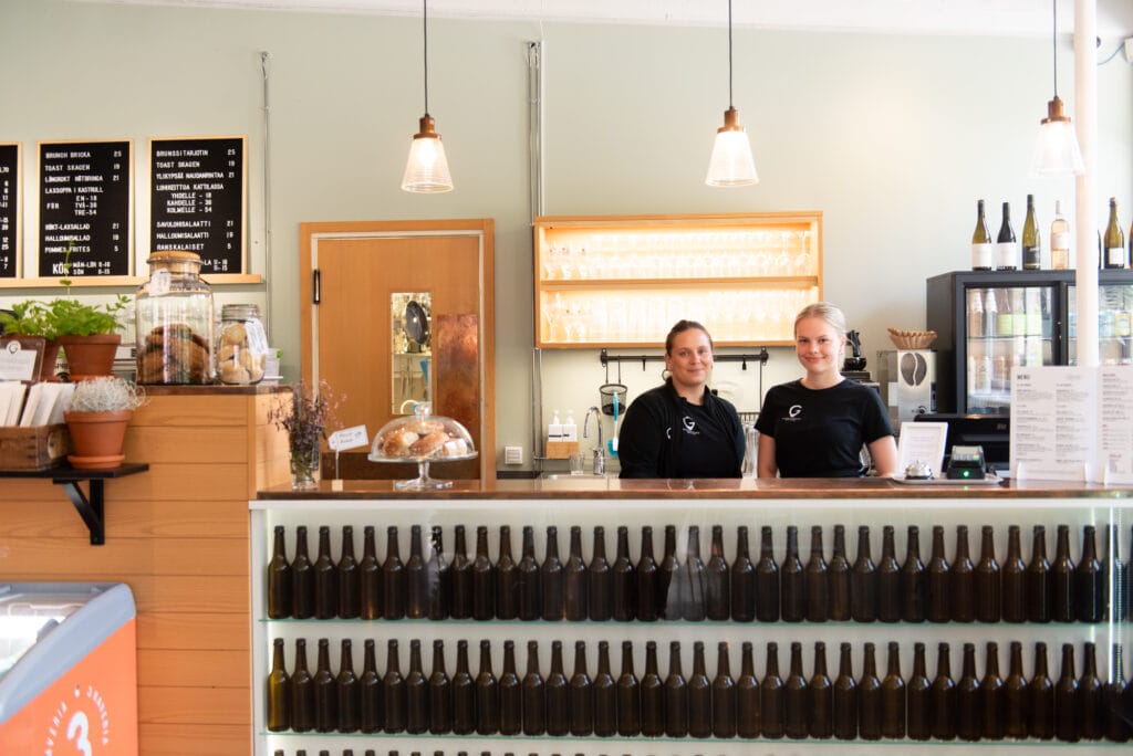 Kahvilan työntekijät tiskin takana, taustalla pulloja.