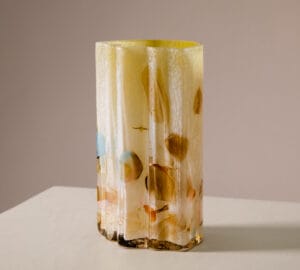 Monivärinen koristeellinen lasimaljakko pöydällä.