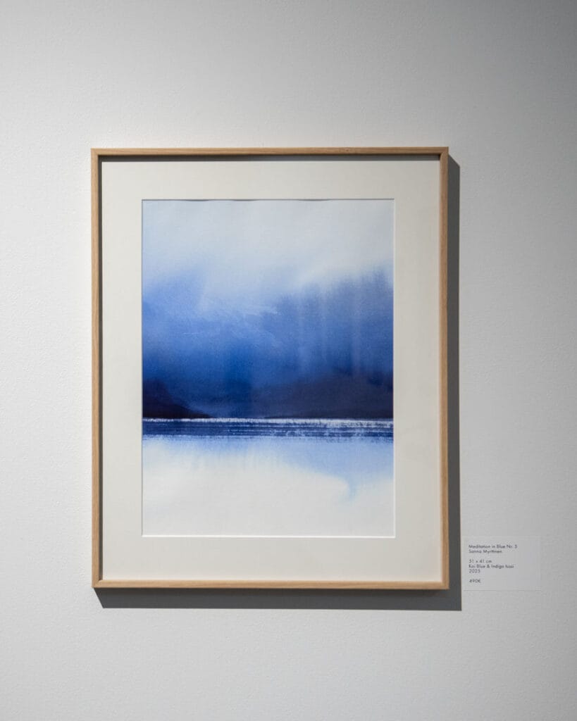 Sininen abstrakti taideteos valkoisella seinällä.