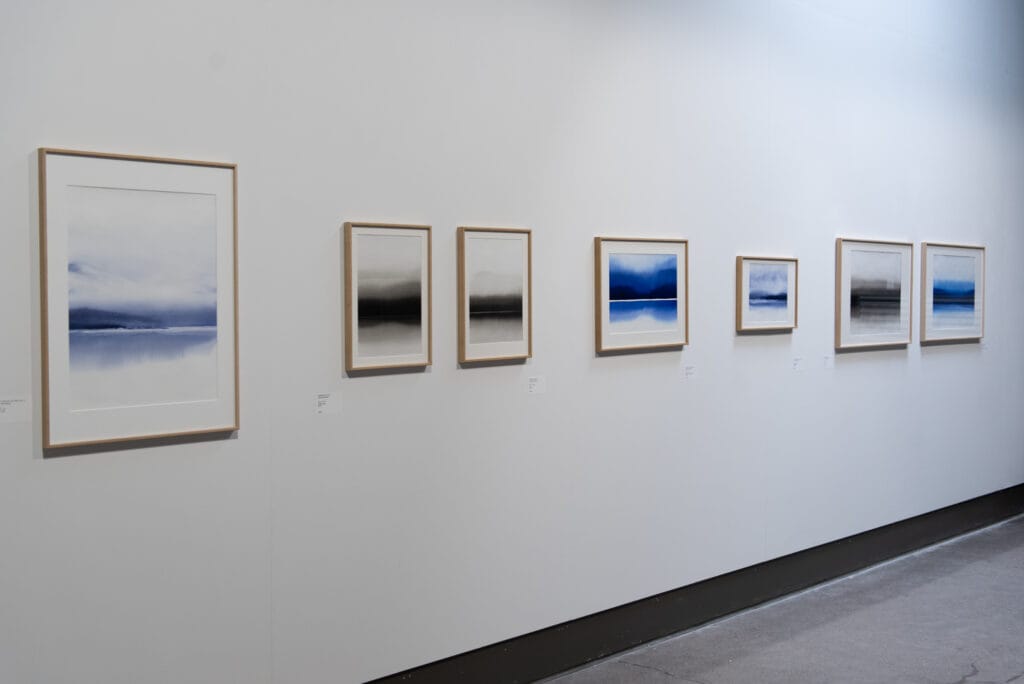 Näyttelyseinällä tauluja sinisävyisin maisemakuvin