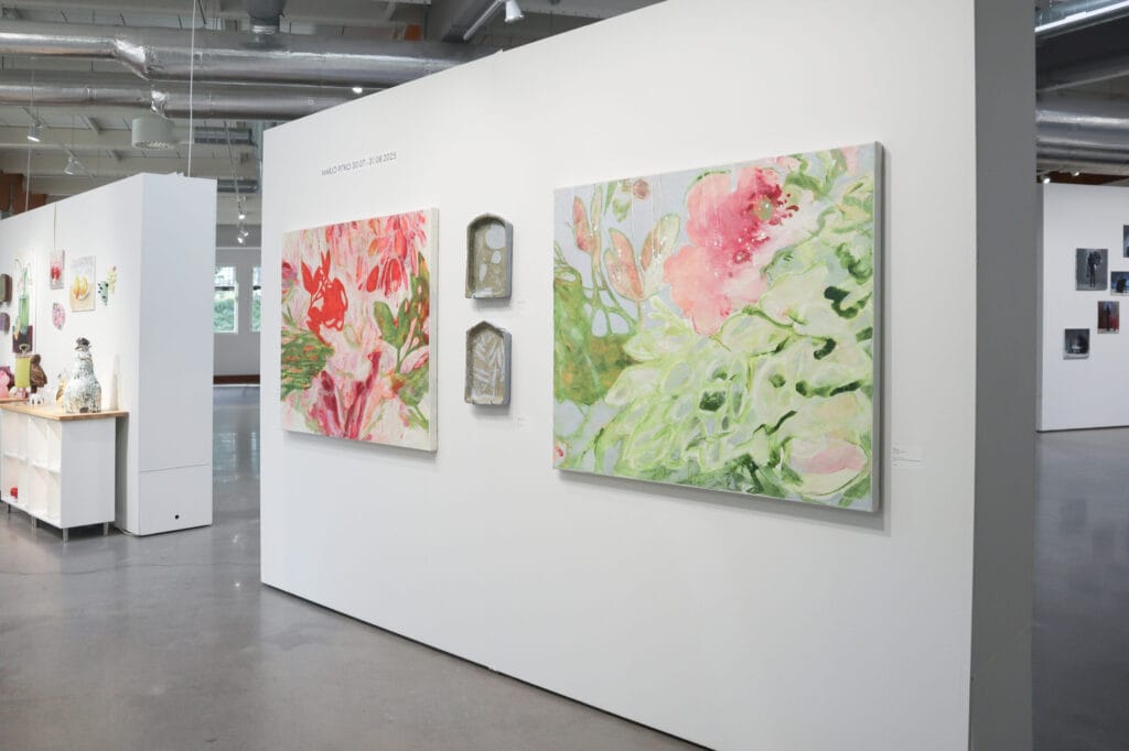 Taidegalleria, värikkäät kukka-aiheiset maalaukset esillä seinällä.