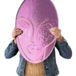 Henkilö pitelee kasvojen muotoista violettia kilpeä.