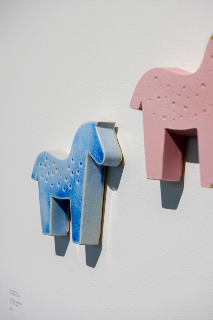 Sininen ja vaaleanpunainen keraaminen hevosveistos seinällä.