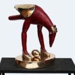 Punainen ja kultainen lintuveistos munan kanssa.