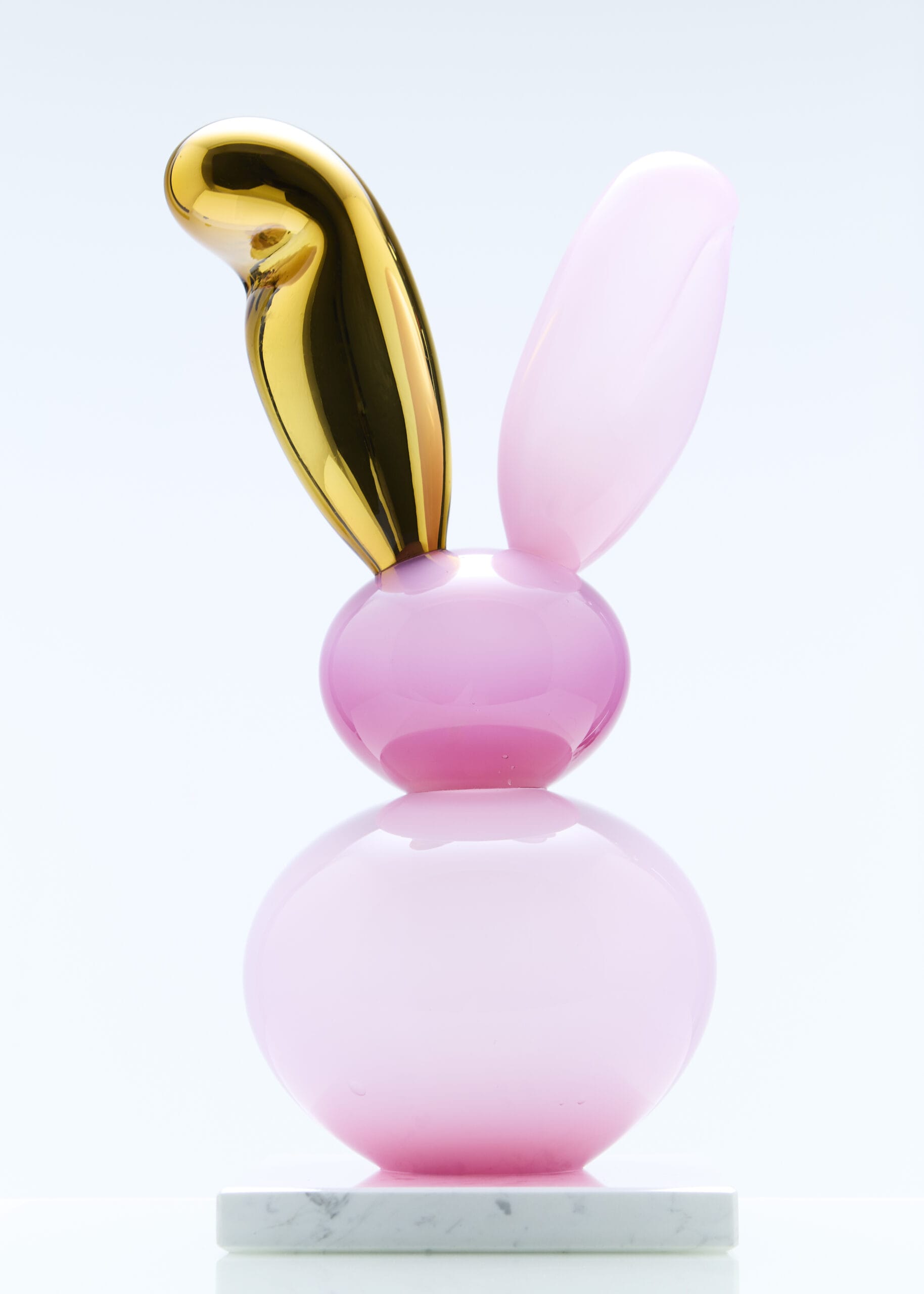 Vaaleanpunainen ja kultainen kaniinipatsas marmorialustalla.