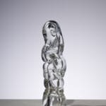 Lasiin kaiverrettu veistos vaimokuvasta valaistussa tilassa.