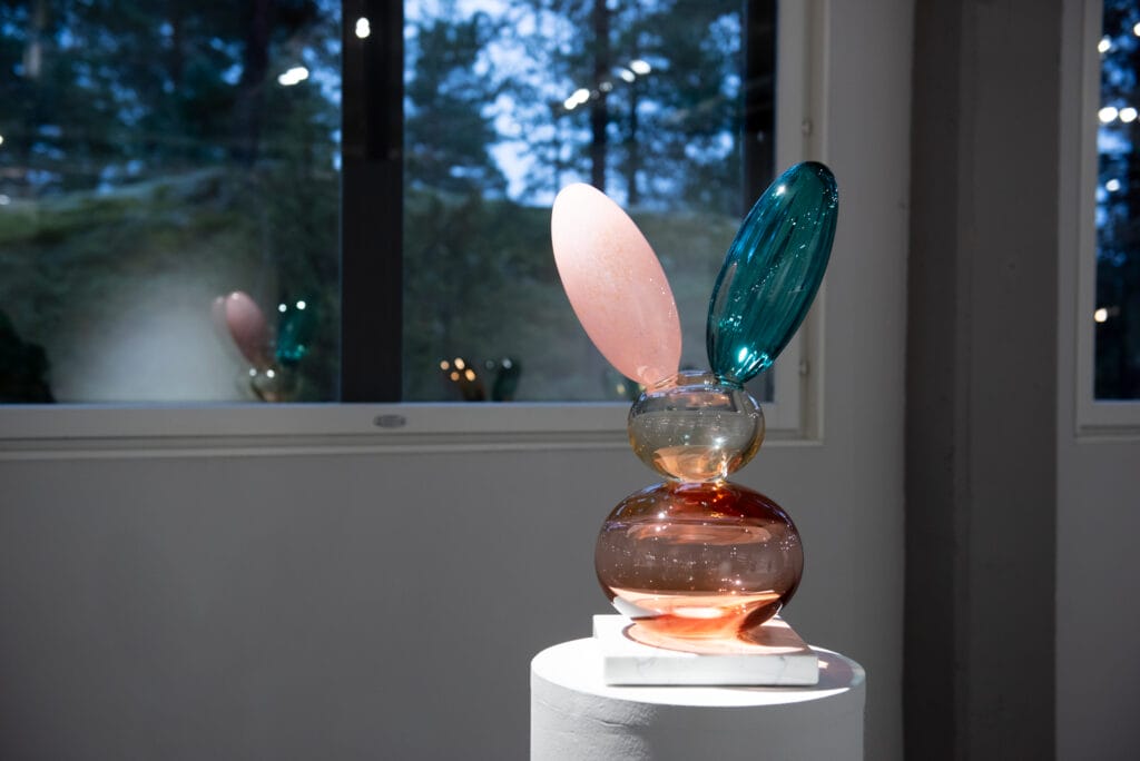 Värikäs lasiveistos ikkunan edessä näyttelyssä.