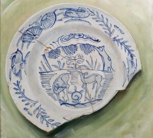 Rikkinäinen posliinilautanen sinisellä kuvioinnilla vihreällä pohjalla.