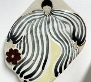 Taiteellinen keramiikkaefekti, mustavalkoraidallinen hahmo, kukka kädessä.