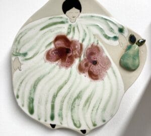 Keraaminen koriste hahmolla ja päärynällä.