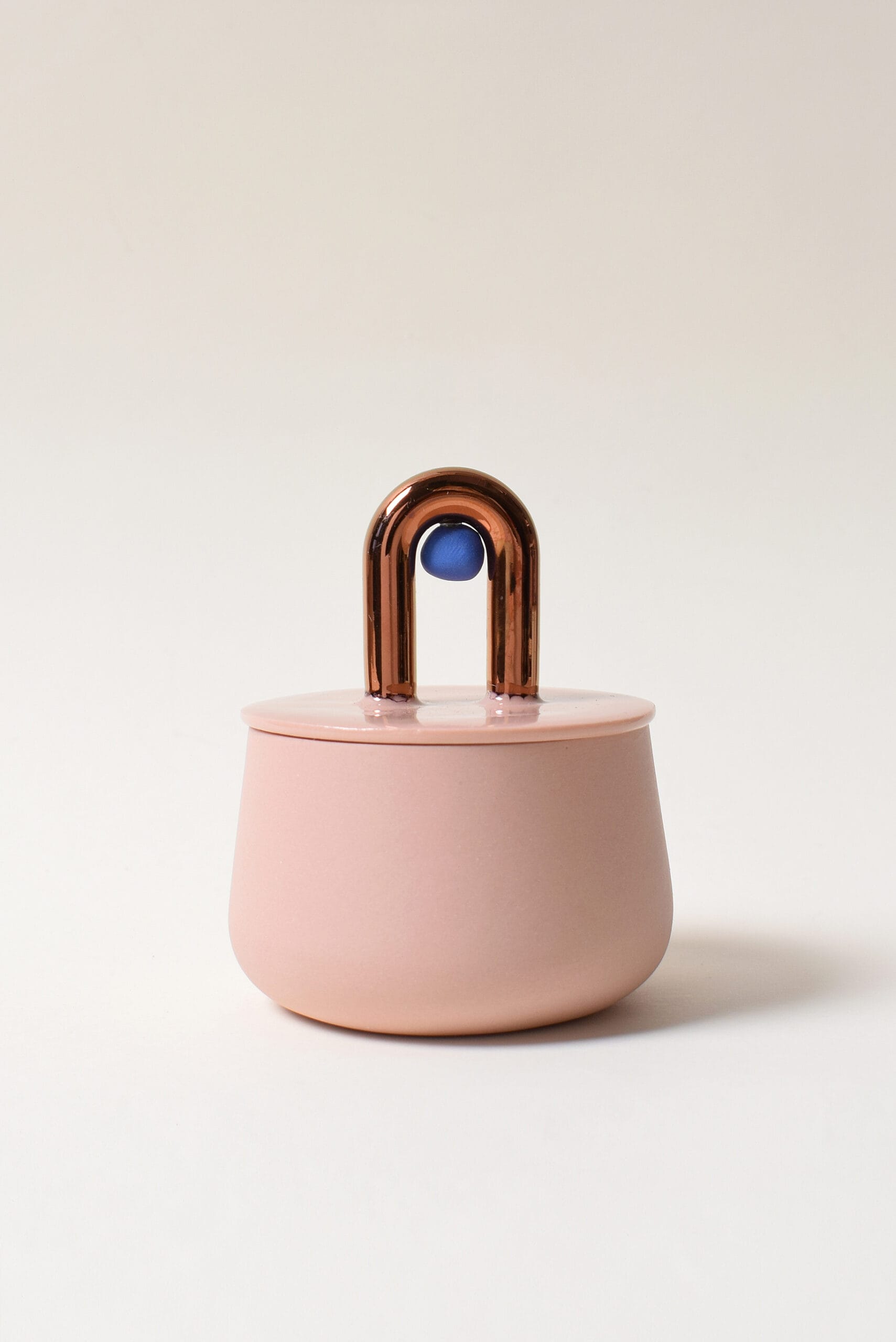Vaaleanpunainen purkki, metallinen kahva ja sininen koriste.