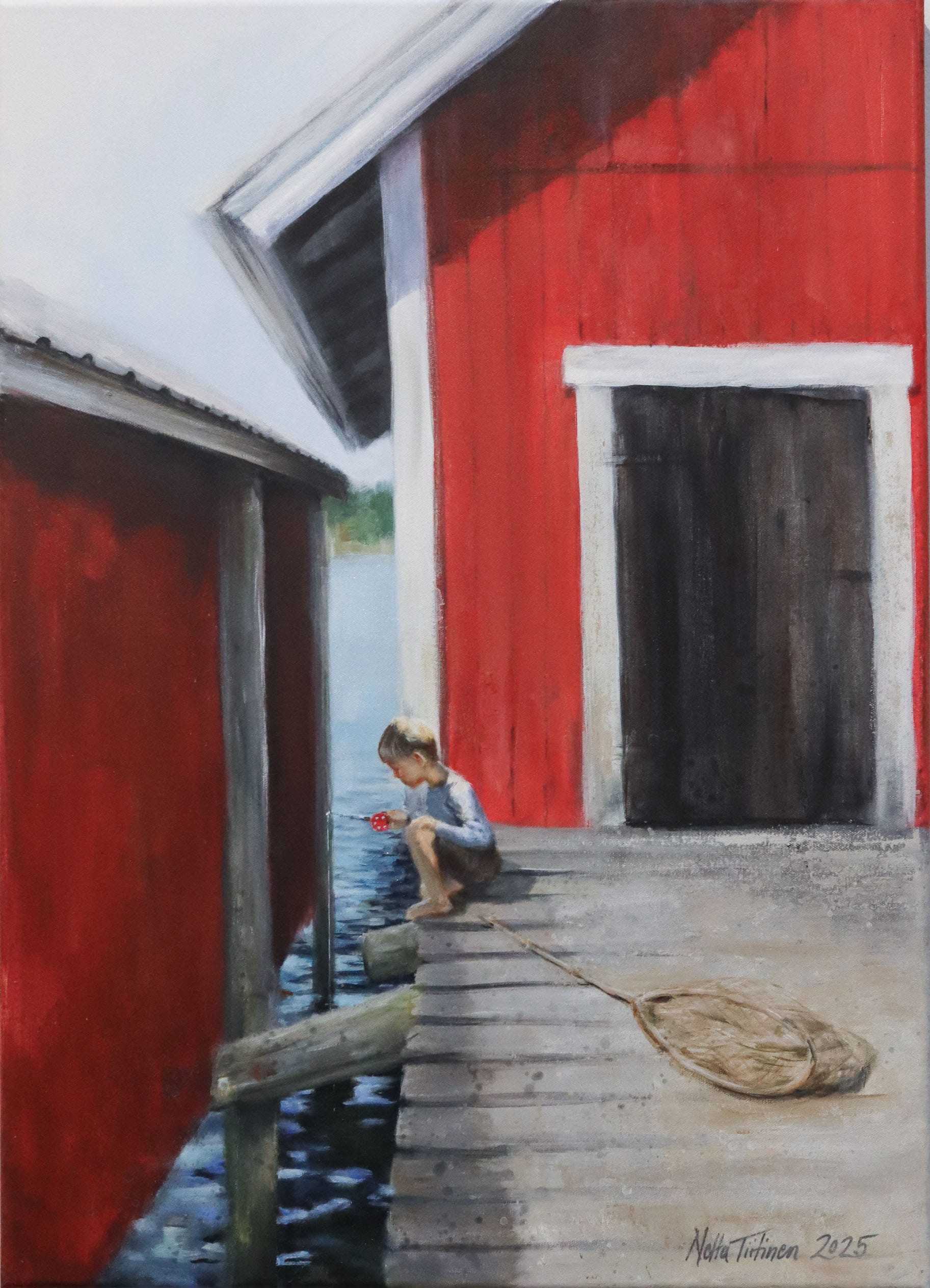 Lapsi istuu laiturilla punaisen mökin vieressä